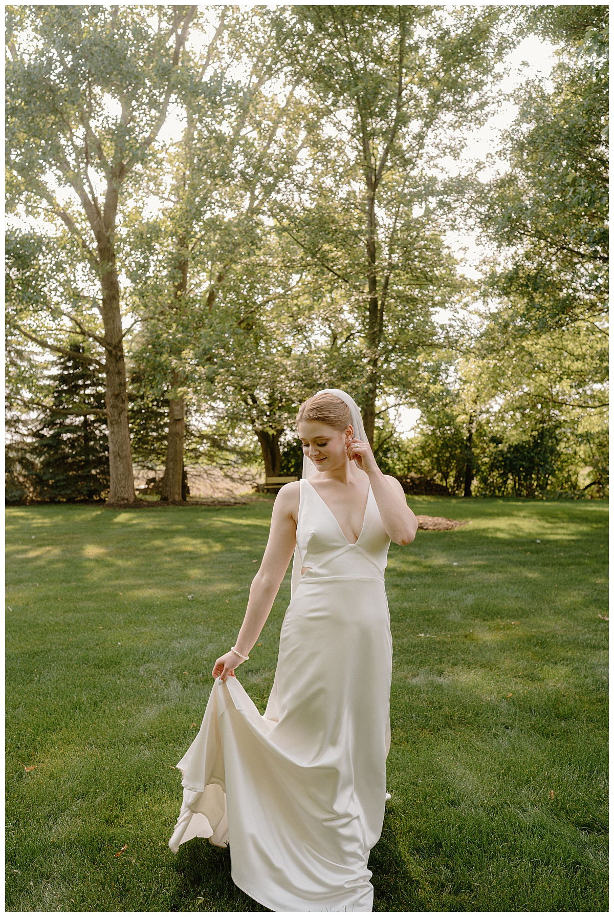 bride holds train and looks down at gown during backyard summer celebration