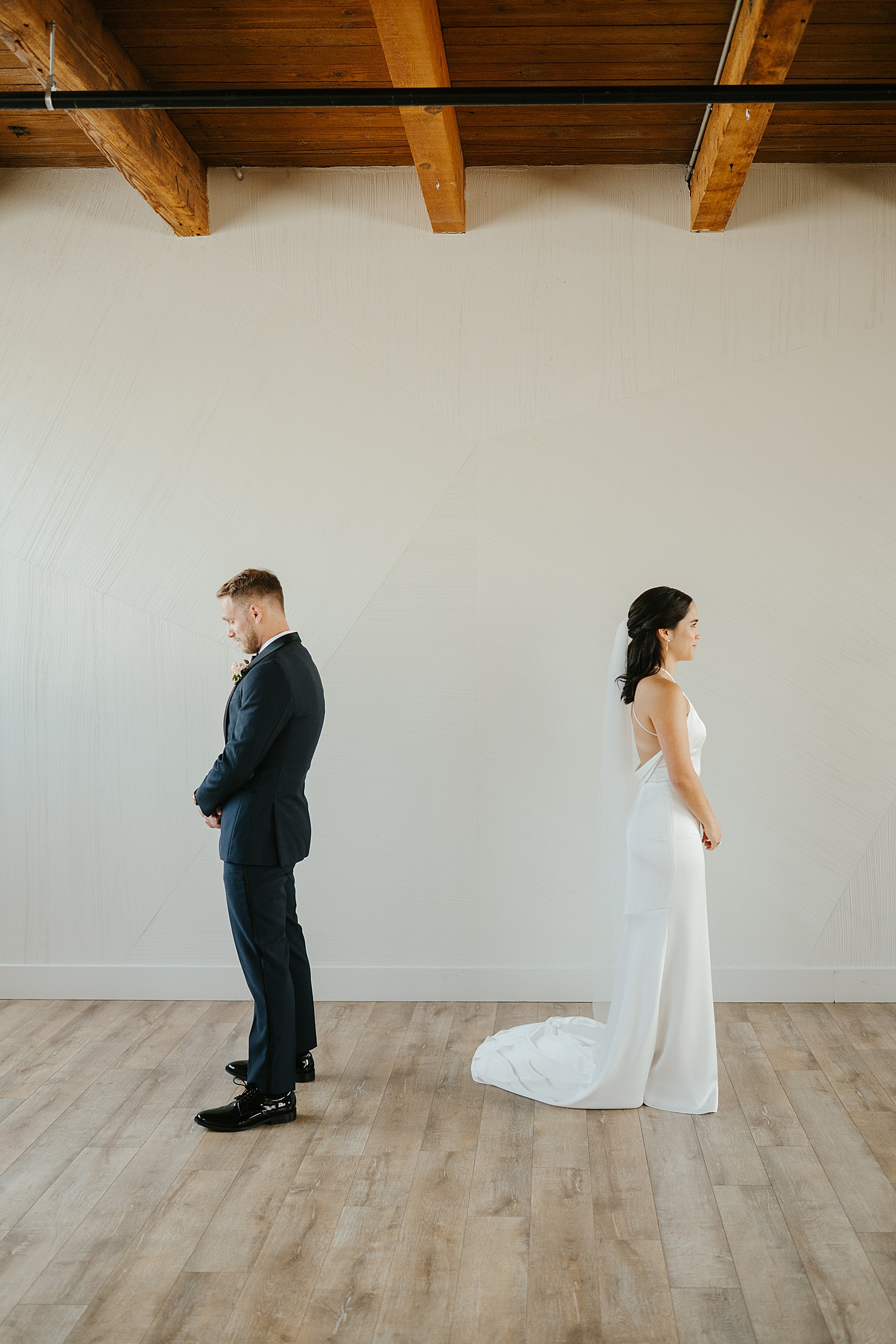 bride and groom stand back to back in blank loft by Morgan McIntire Photography
