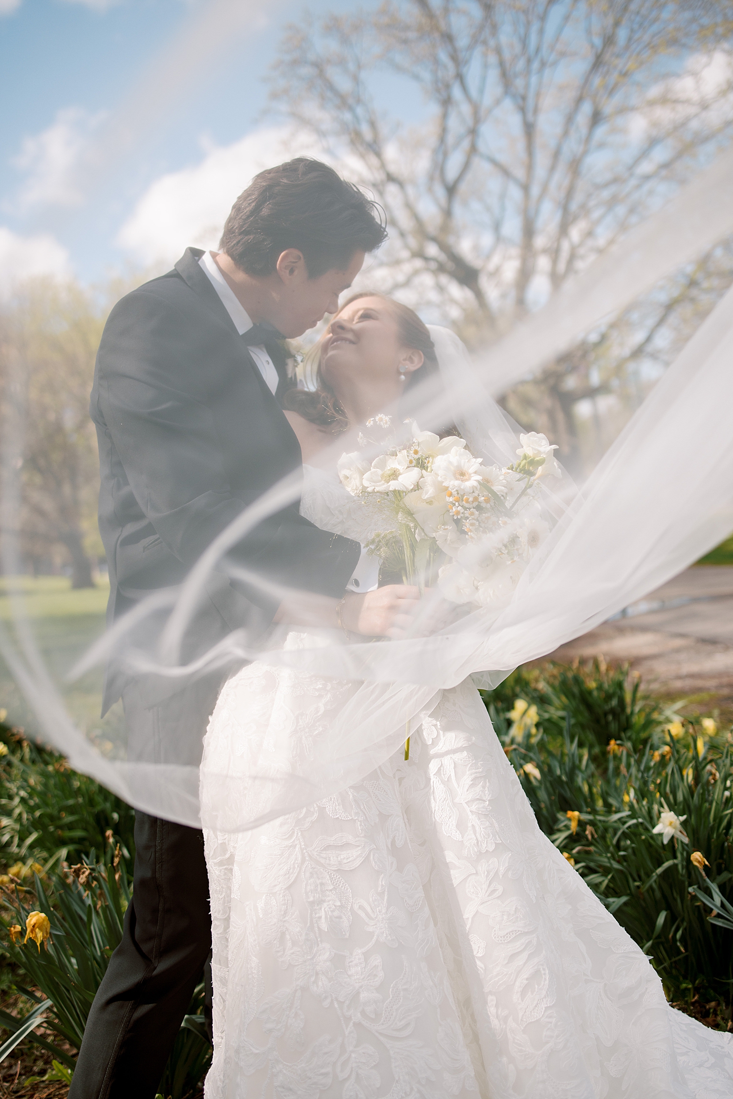 man leans in to kiss his new wife as her veil whips around by Chicago wedding photographer